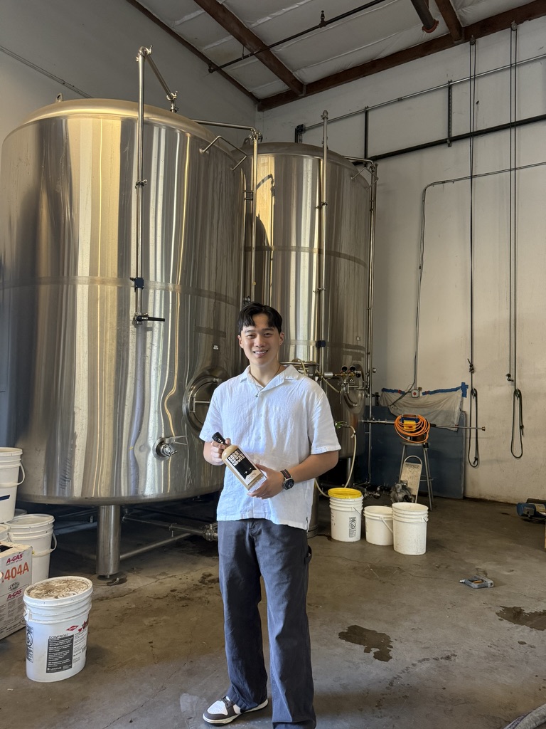 Brandon Hoang with a Boba After Hours bottle in front of the distillery tanks